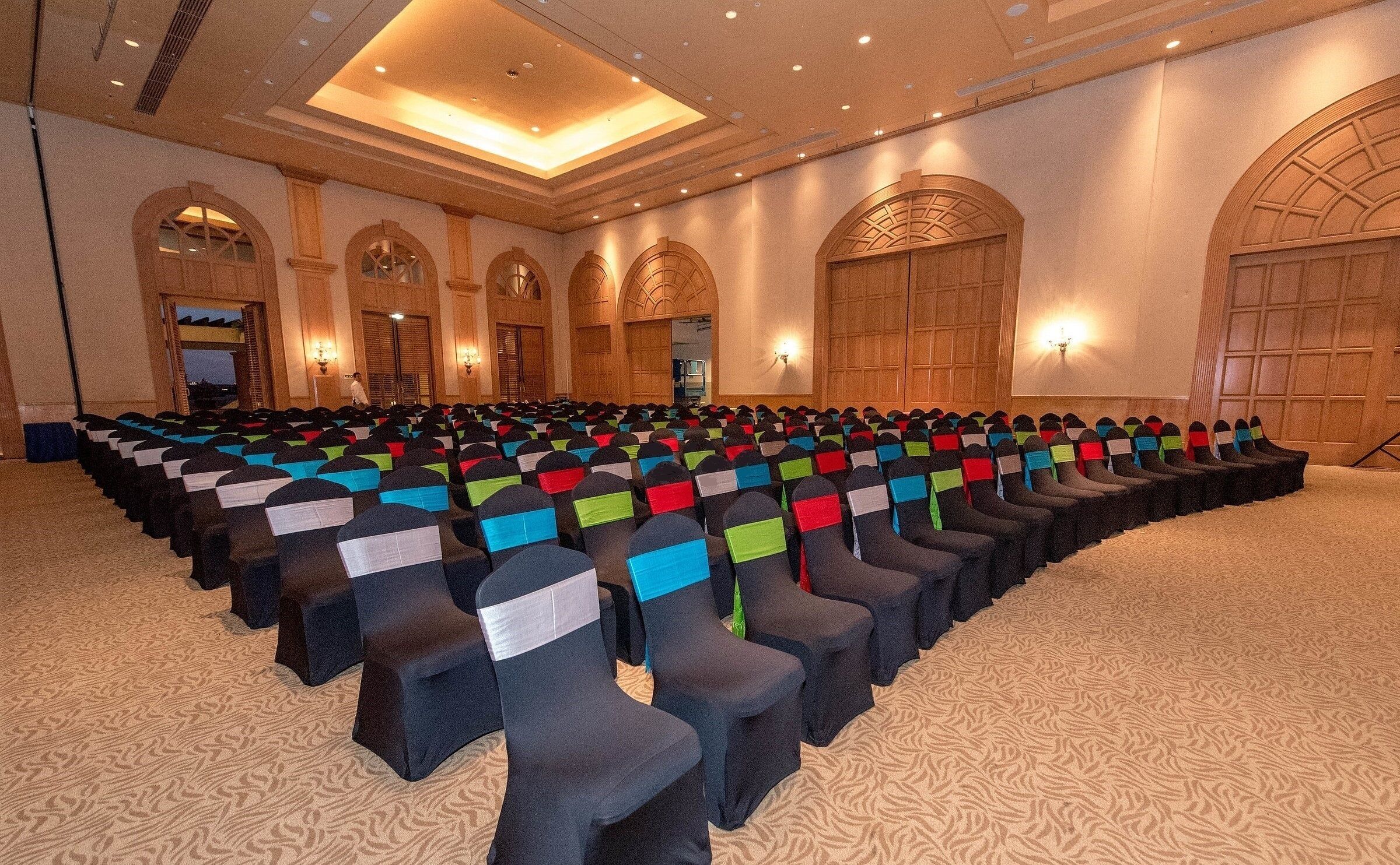 A conference room with rows of chairs, arched doorways, and a patterned carpet.