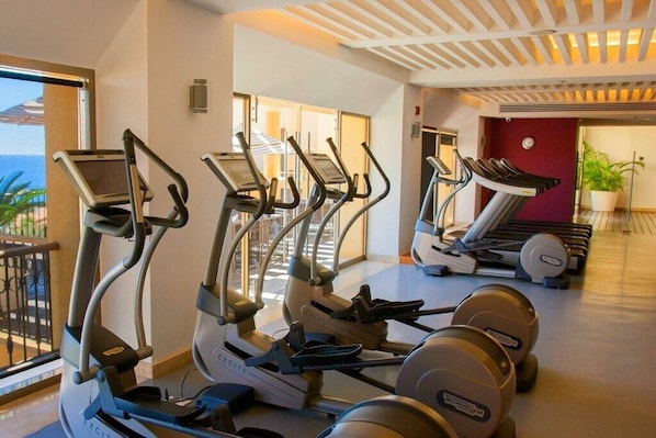 A fitness center with multiple cardio machines, including treadmills and elliptical trainers, and a weight bench area.