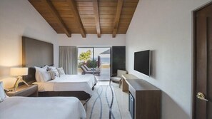 A hotel room with two beds, a desk, a TV, and a view of the beach.