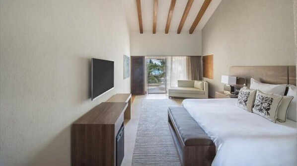 A modern hotel room with a large bed, a flat-screen TV, a sofa, and a view of the outdoors.
