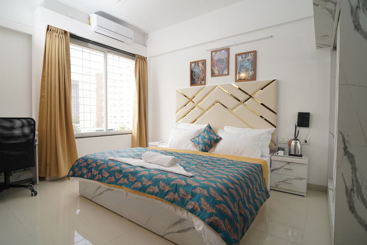 Une chambre d’hôtel avec un lit, un bureau, une chaise, une fenêtre avec des rideaux et des œuvres d’art accrochées au mur.