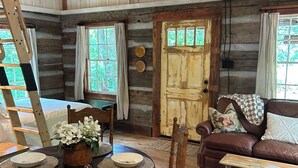 Ein rustikales Blockhaus-Interieur mit Esstisch, Stühlen, einer Couch und einem Deckenventilator.