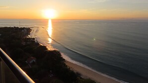 Un atardecer sobre una playa con vista despejada del océano y una costa distante.