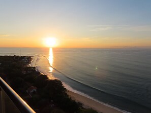 Un atardecer sobre una playa con vista despejada del océano y una costa distante.