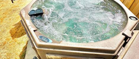A hot tub with a stone base, surrounded by a wooden fence, and equipped with a control panel.
