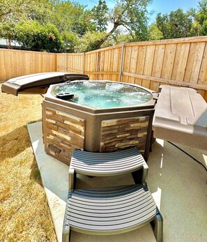 A hot tub with a stone facade and two lounge chairs. - Cozy 3 bed home, grill, hot tub, garage, EV, pet friendly (Fort Worth)