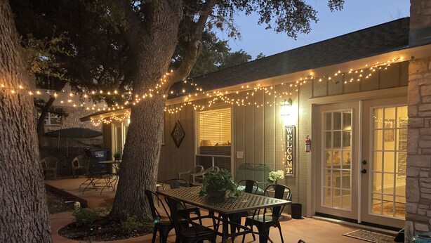 An outdoor patio with a table and chairs, string lights, and a stone wall.