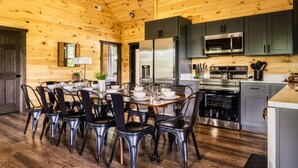 A wooden cabin interior with a dining area, kitchen, and a large window. - Fall Mtn Escape! HeatedPool-HotTub-Theater-Views (Sevierville)