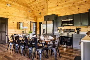 A wooden cabin interior with a dining area, kitchen, and a large window.