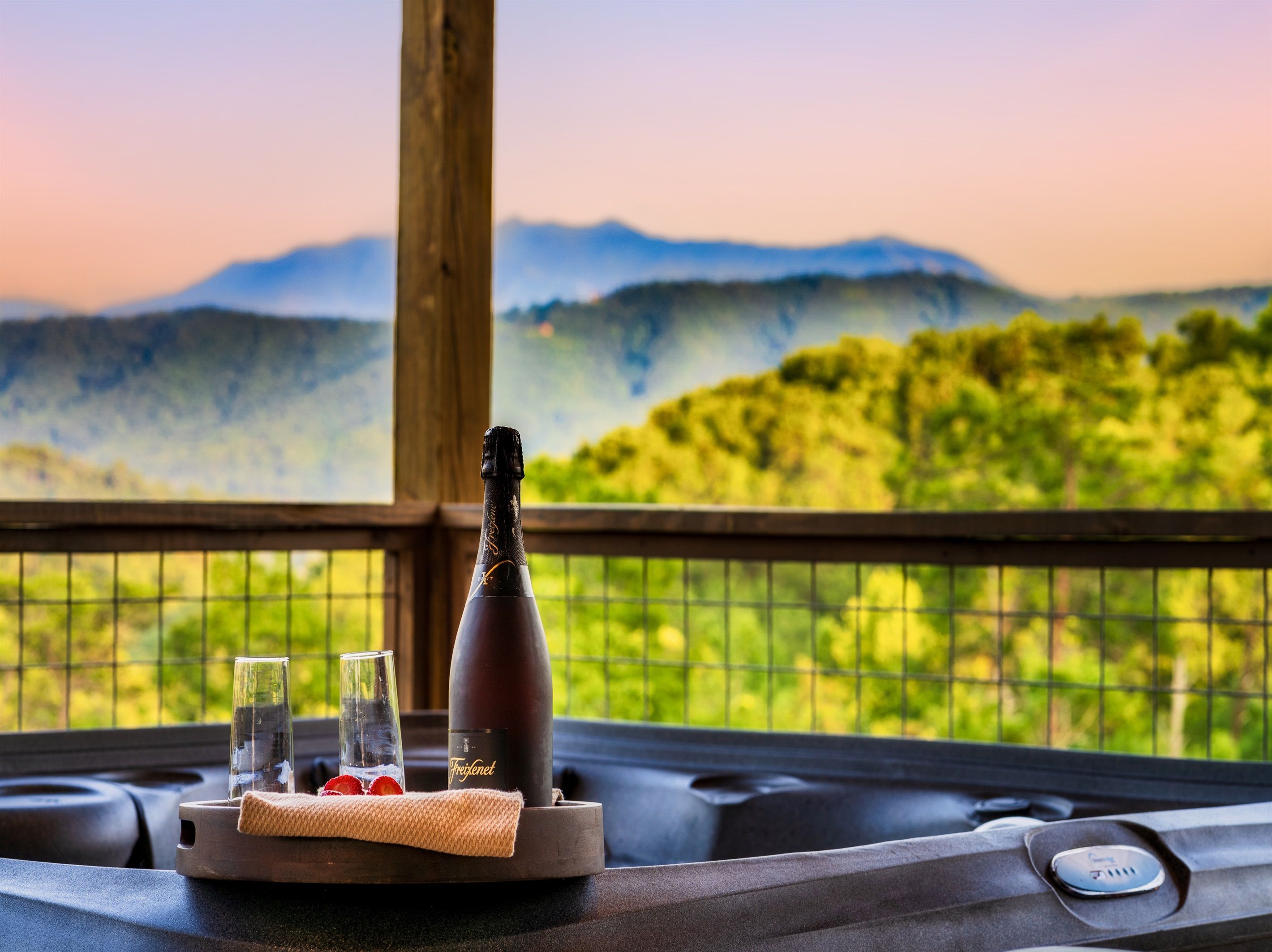 Una vasca idromassaggio con una bottiglia di Freixenet champagne, due bicchieri e un asciugamano su un basamento di legno.