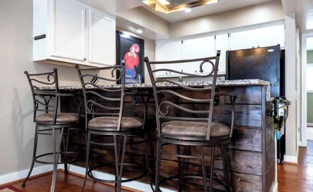 A kitchen with white cabinets, a dark wooden island, and four metal bar stools.