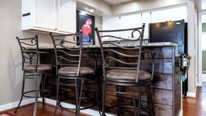 Une cuisine avec des armoires blanches, un îlot central en bois foncé et quatre tabourets de bar en métal.