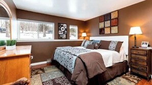 Une chambre à coucher comprenant un lit, des tables de chevet, une commode et une fenêtre donnant sur des arbres.