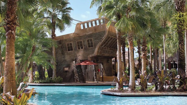Un resort con piscina, palmeras y un edificio de estilo arquitectónico singular.