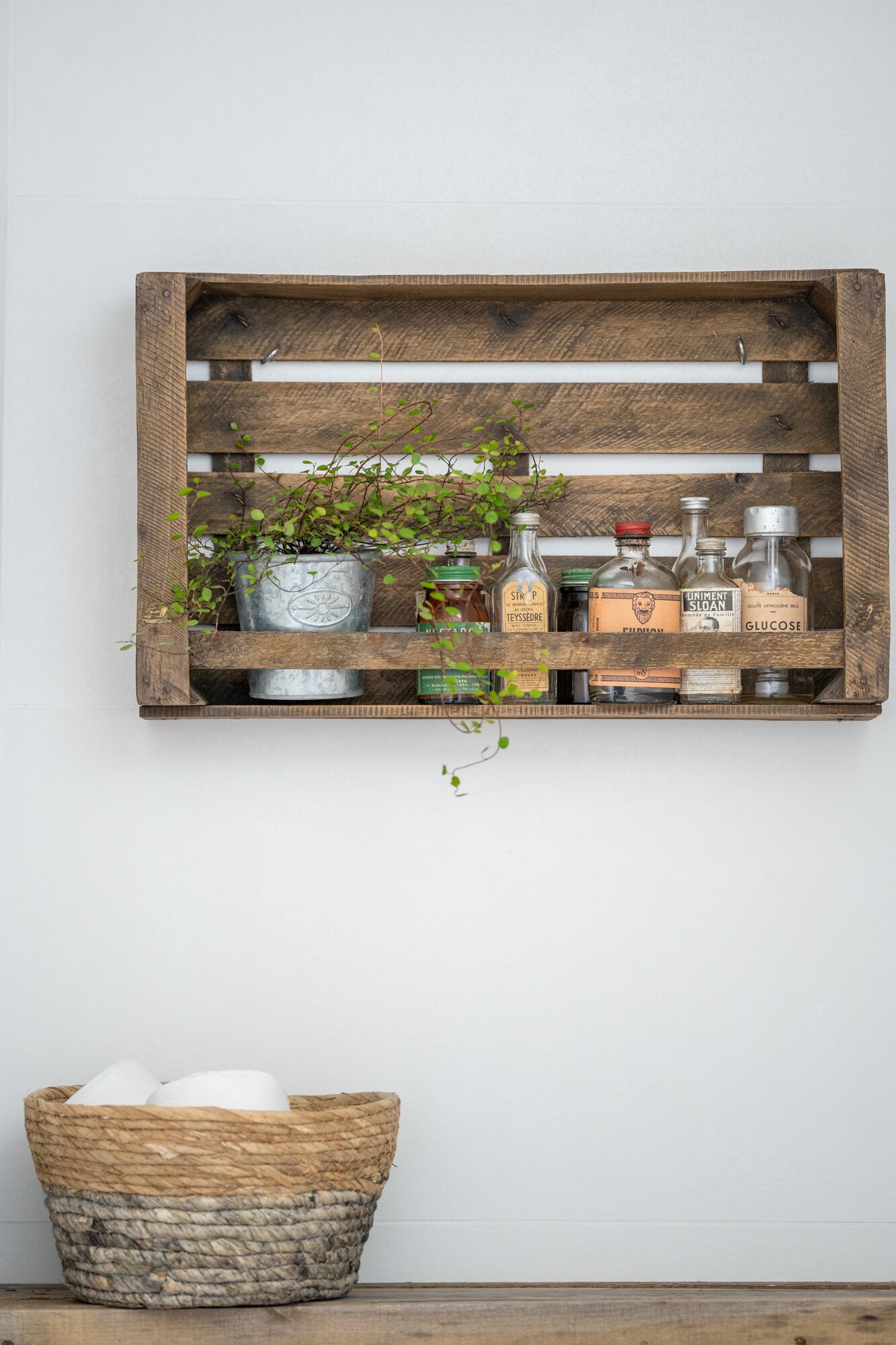 A rustic wooden shelf with various glass bottles and a woven basket below.