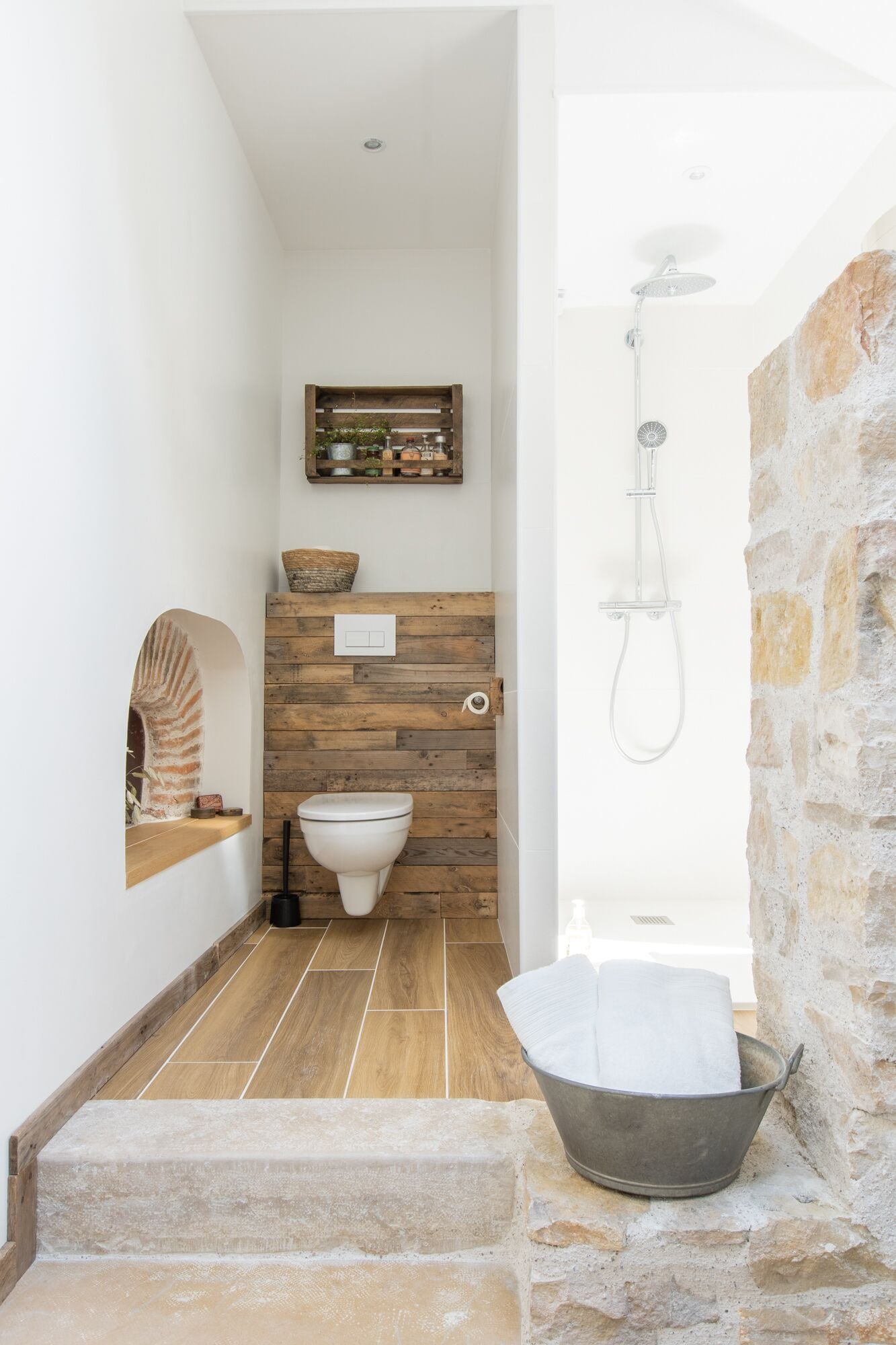Een badkamer met een houten wand, een wit toilet, een douche en een stenen wand.