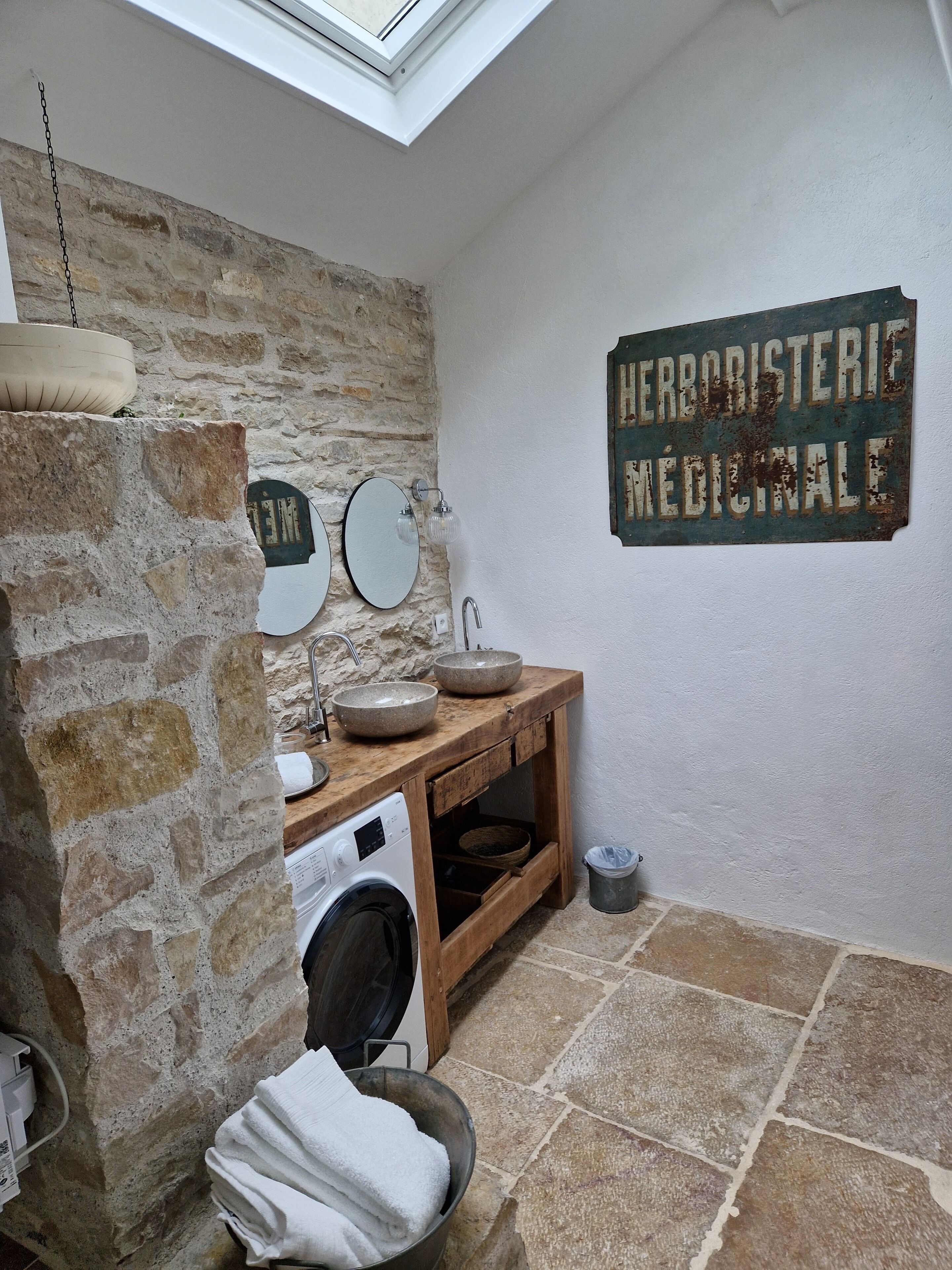 A rustic bathroom with a stone wall, wooden vanity, and a skylight.
