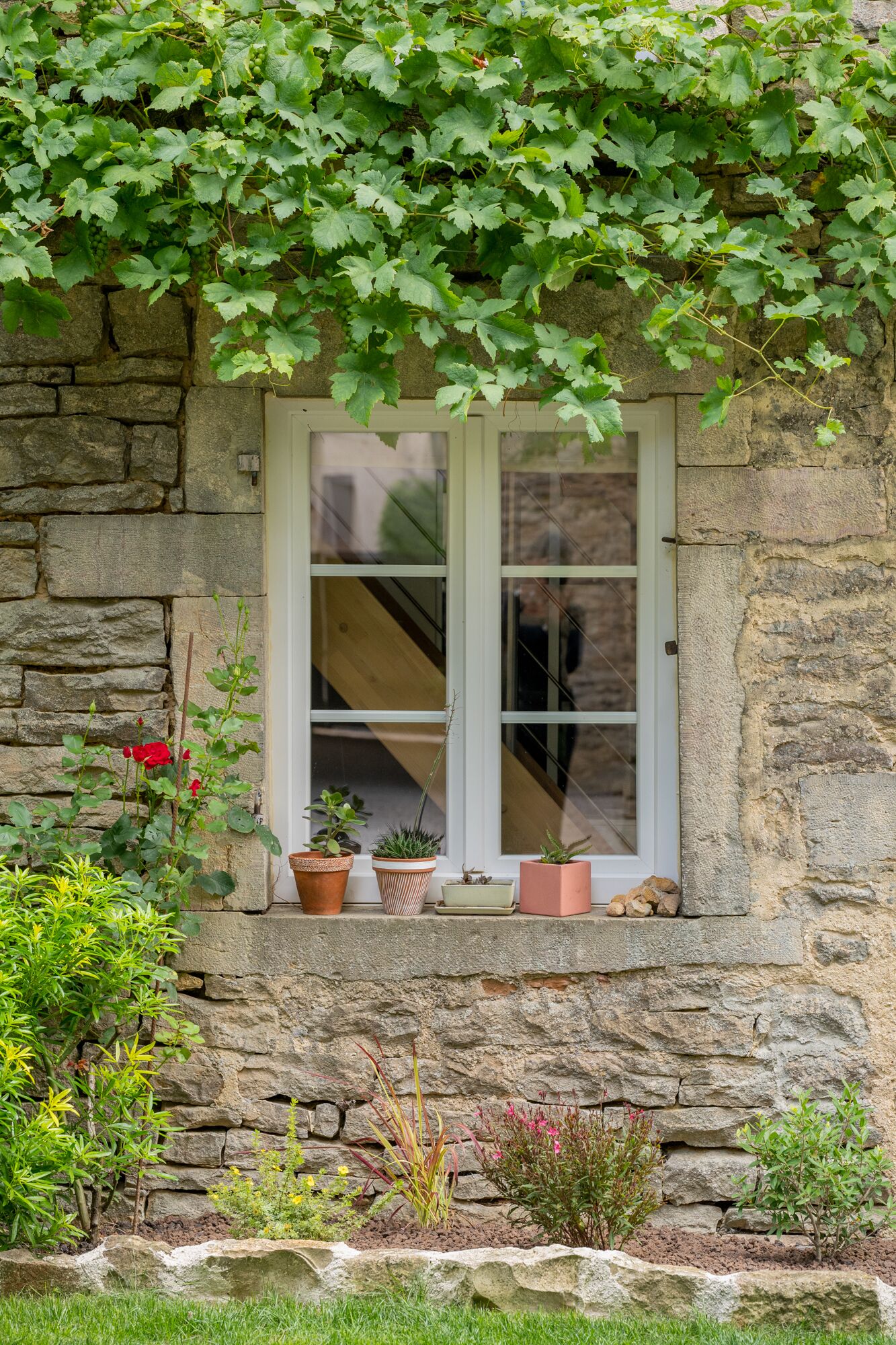 Un bâtiment en pierre avec une fenêtre, des plantes en pot et un jardin.