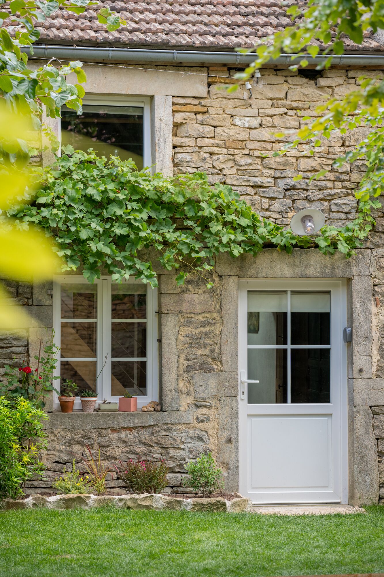 Una casa de piedra con puerta y ventanas blancas, rodeada de un jardín bien cuidado.