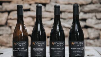 Quatro garrafas de vinho com etiquetas, dispostas sobre uma superfície de madeira, com um muro de pedra ao fundo.