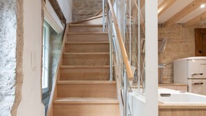 Eine Holztreppe mit Metallgeländern führt zu einem Küchenbereich mit einer Steinwand und einem Fenster.
