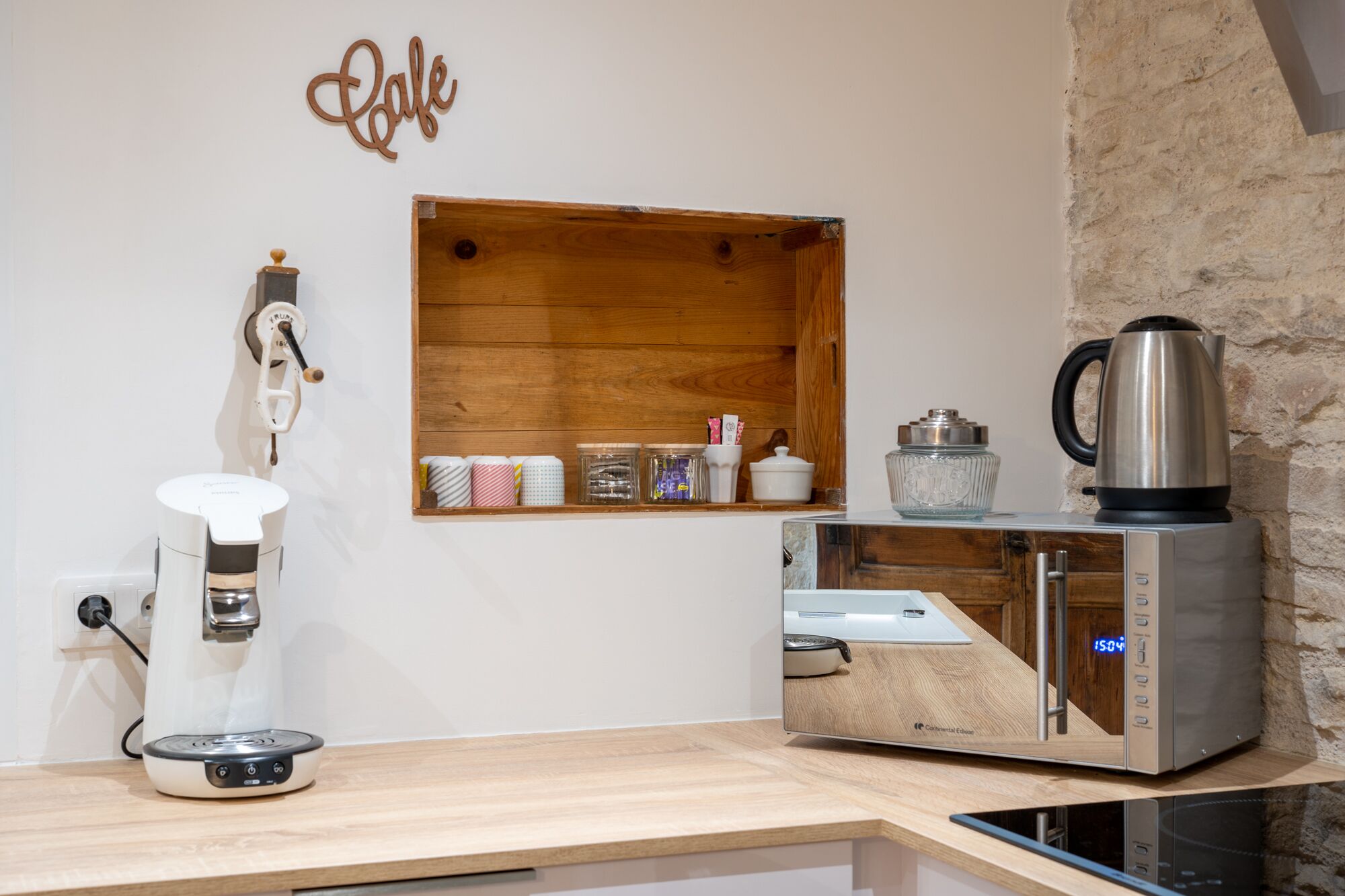 A kitchen with a coffee maker, a kettle, and a wooden shelf with jars.