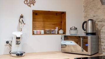 A kitchen with a coffee maker, a kettle, and a wooden shelf with jars.