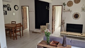 Un saló amb televisió sobre un suport de fusta, un sofà, una taula de menjador amb cadires i una xemeneia.