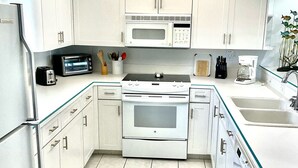 Una cocina moderna con gabinetes blancos, microondas, estufa y ventilador de techo.