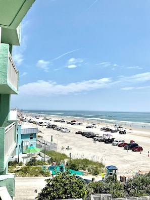 Vista de la playa con un estacionamiento, sombrillas y una torre de salvavidas.