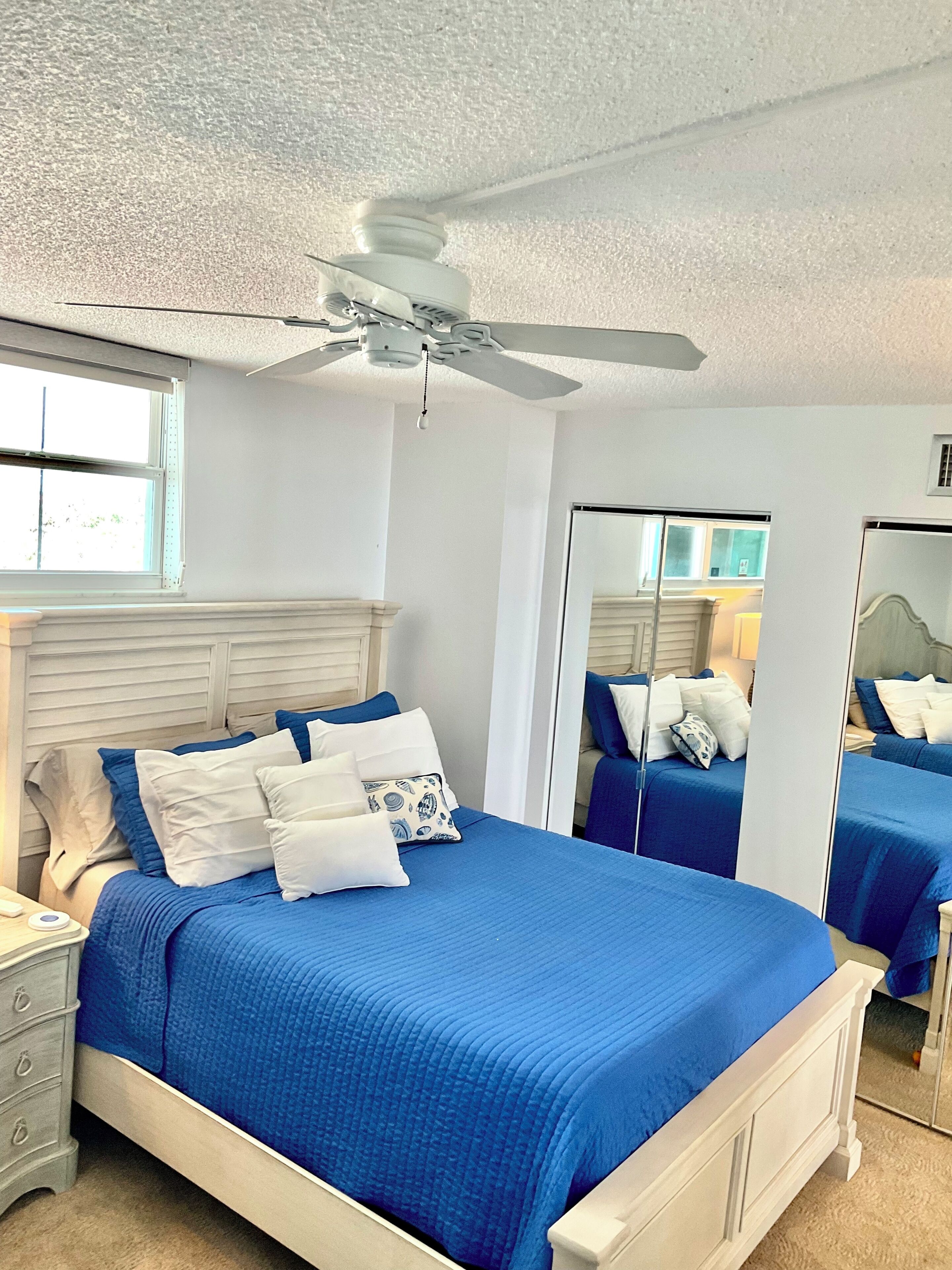 A bedroom with a large bed, a ceiling fan, and a window.