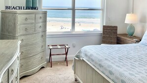 Un dormitorio con vista a la playa, un ventilador de techo, un aparador, una cama y una mesita de noche con una lámpara.