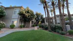 A residential building with a well-maintained lawn, palm trees, and flowering shrubs. - Gorgeous Lakeview Resort Style Condo (Phoenix)