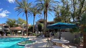 A swimming pool area with lounge chairs, a table with a blue umbrella, and palm trees. - Gorgeous Lakeview Resort Style Condo (Phoenix)