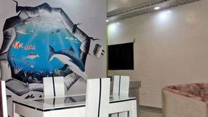 A dining area with a table and chairs, a wall mural depicting an underwater scene with fish and a shark, and a patterned sofa in the background. - Appart'hôtel & bar-restaurant Maëlys (Gagnoa)
