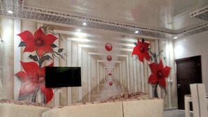 A hallway with a TV screen, red flower paintings, and a seating area with beige sofas. - Appart'hôtel & bar-restaurant Maëlys (Gagnoa)