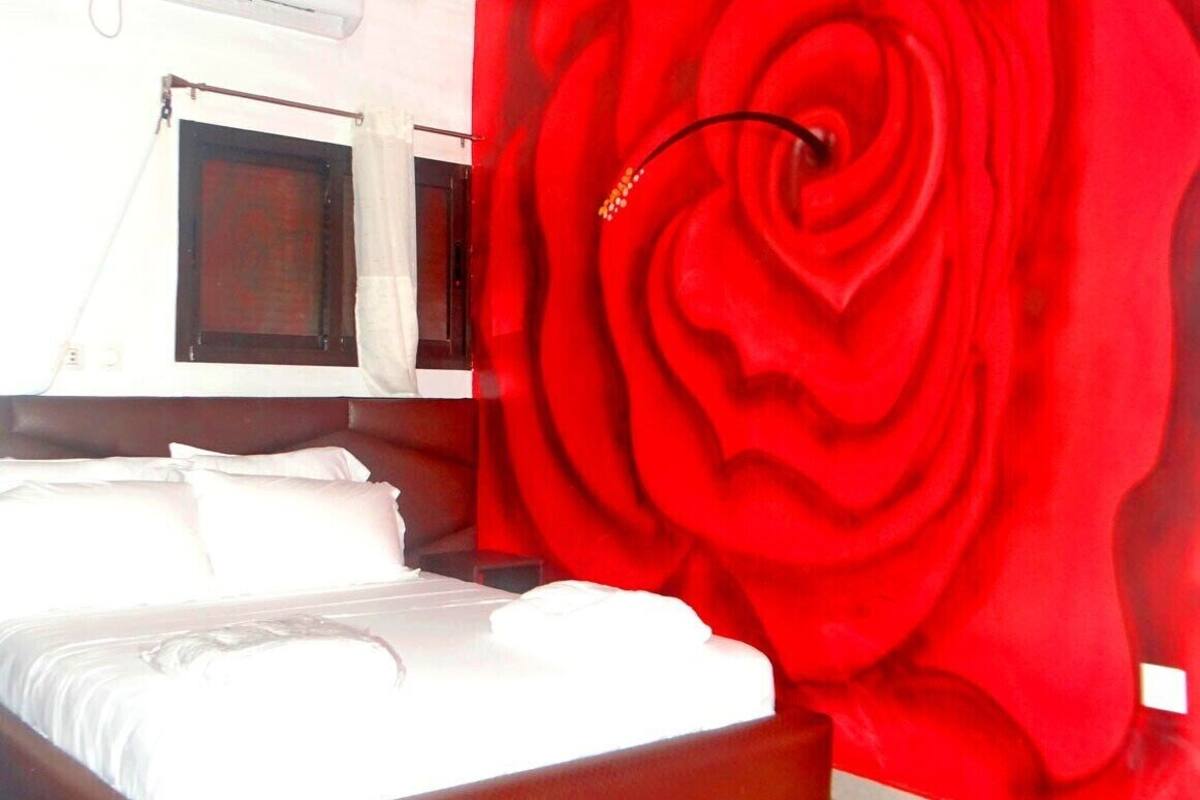 A hotel room with a bed, a window with a curtain, and a red floral wall design.