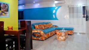 A modern living area with a blue accent wall, a sectional sofa, and a dining table with chairs. - Appart'hôtel & bar-restaurant Maëlys (Gagnoa)