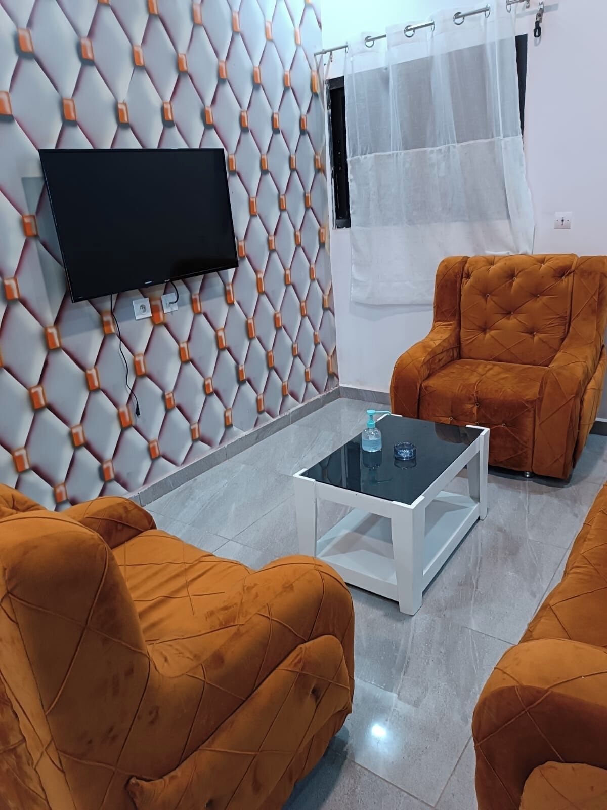 Una sala de estar con un diseño geométrico moderno en la pared, un televisor de pantalla plana montado y dos sillones a juego con una mesa de centro de vidrio.