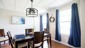 A dining area with a wooden table, chairs, a chandelier, and a window with curtains.