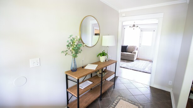 A hallway with a wooden console table, a mirror, a vase with a plant, a lamp, and a door leading to a living room.