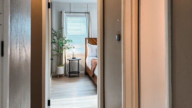 Un pasillo que conduce a un dormitorio con una cama, una mesita y una planta en maceta.