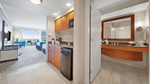 A modern hotel room with a kitchen area, a dining area, and a large window offering a view.