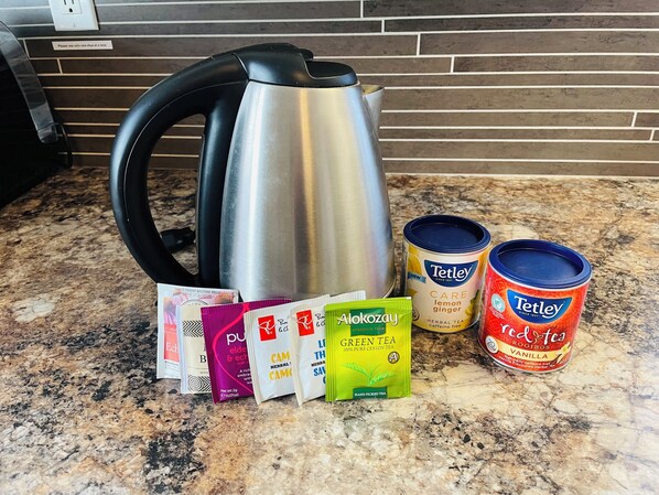 Una encimera de cocina con un hervidor, bolsitas de té y latas de té.
