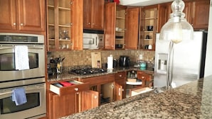 Una cocina con armarios de madera, encimeras de granito, electrodomésticos de acero inoxidable y una lámpara colgante.