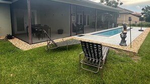 A modern house with a glass-enclosed patio, a swimming pool, and outdoor furniture.
