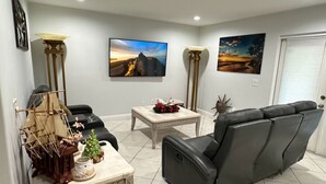 A living room with a sofa, a coffee table, and two floor lamps. There are two paintings on the wall and a television.