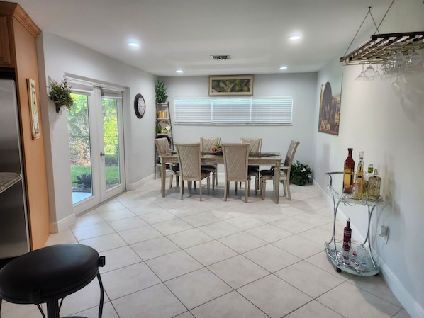 A dining area with a table and chairs, a glass cabinet with bottles, and a clock on the wall. - Endless Summer 7 min walk to the peaceful white sand beach. 3 bedrooms, 2 baths. (Marco Island)