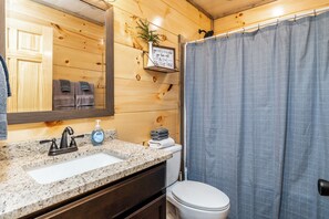 Et badeværelse med vask med granitbordplade, et spejl, et toilet og en brusekabine.