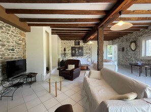 A cozy living room with stone walls, a flat-screen TV, a glass coffee table, a sofa, and a wooden ceiling. - CHEZ CAZALETS - SUSMIOU (SUSMIOU)